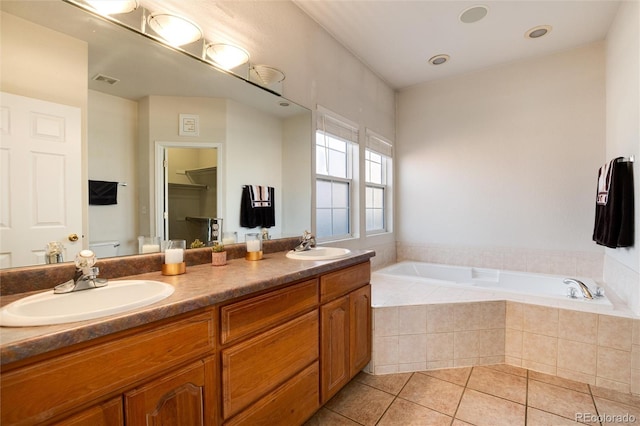 bathroom featuring tiled tub, vanity, and tile patterned flooring