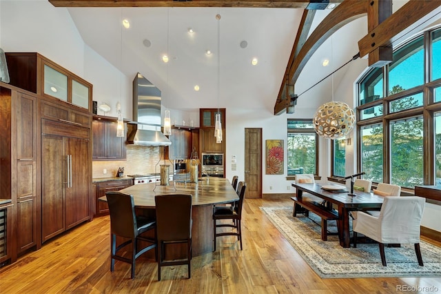 kitchen with wall chimney exhaust hood, built in appliances, a center island, and light hardwood / wood-style floors