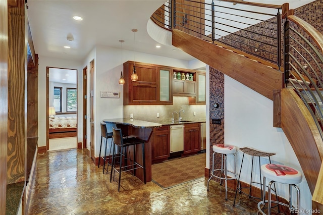 kitchen with sink, stainless steel dishwasher, a kitchen breakfast bar, light stone countertops, and backsplash