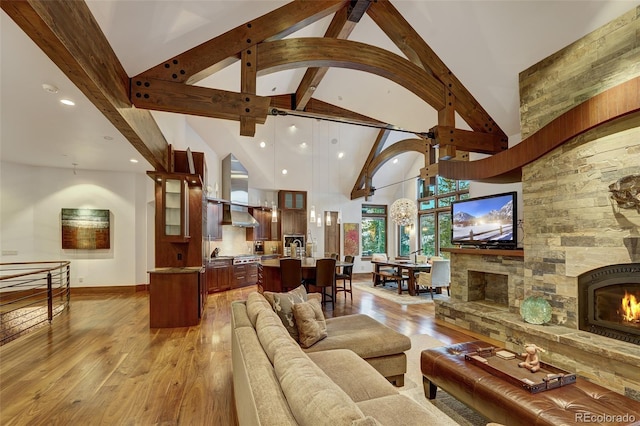 living room with a fireplace, high vaulted ceiling, beamed ceiling, and light wood-type flooring