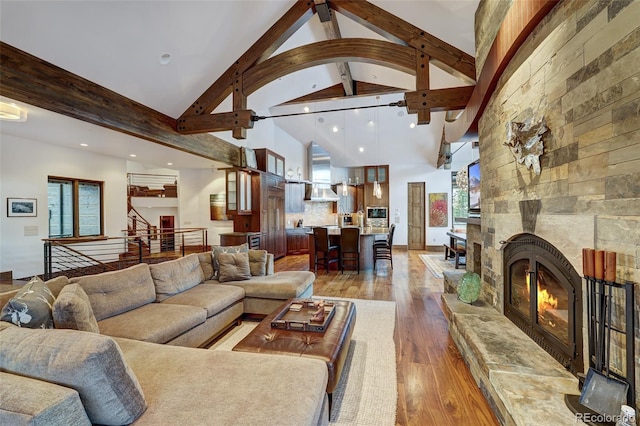 living room with wood-type flooring, high vaulted ceiling, a large fireplace, and beamed ceiling