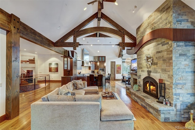 living room featuring high vaulted ceiling, beam ceiling, light hardwood / wood-style floors, and a stone fireplace