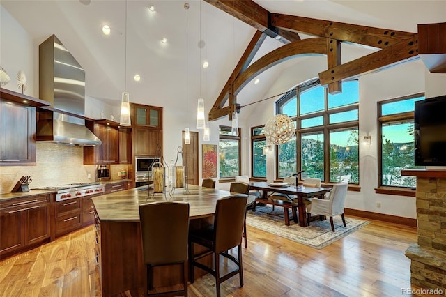 kitchen featuring pendant lighting, backsplash, stainless steel gas cooktop, an island with sink, and light wood-type flooring