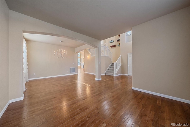 6317 Ruby Hill Dr, Erie, CO 80516 - unfurnished living room featuring an inviting chandelier, wood-type flooring, visible vents, stairway, and arched walkways