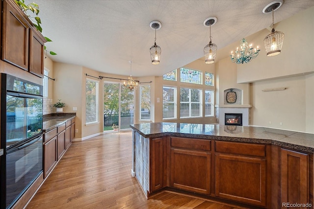 6317 Ruby Hill Dr, Erie, CO 80516 - kitchen with hanging light fixtures, light wood finished floors, dobule oven black, a chandelier, and a glass covered fireplace
