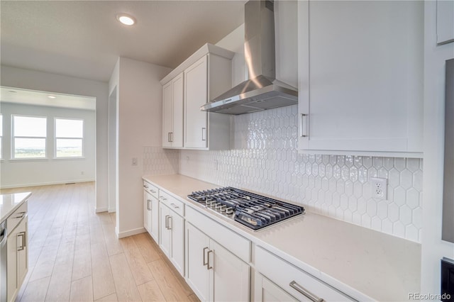 kitchen featuring stainless steel gas cooktop, tasteful backsplash, light wood-type flooring, wall chimney range hood, and white cabinets