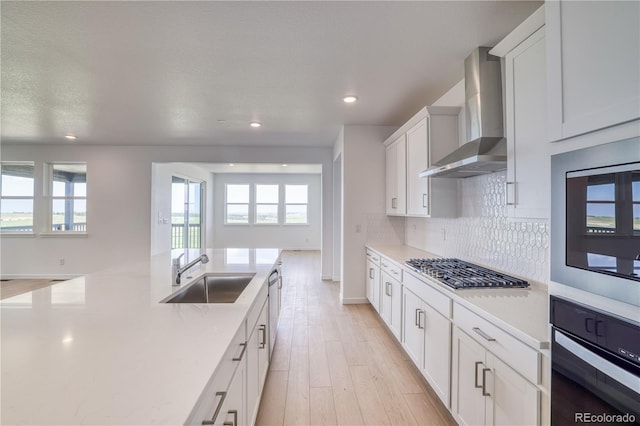 kitchen featuring sink, appliances with stainless steel finishes, wall chimney range hood, decorative backsplash, and white cabinets