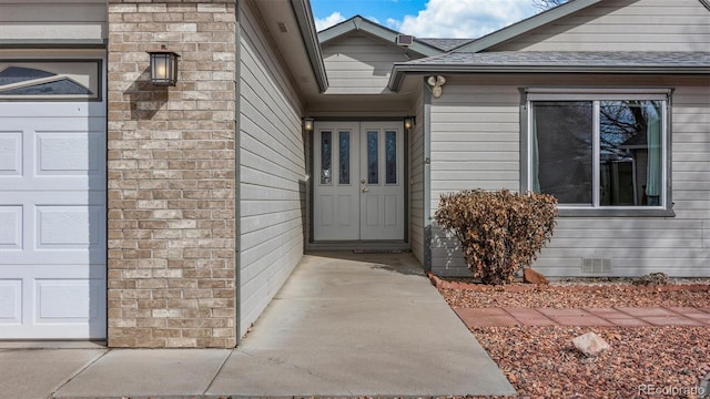 view of exterior entry with a garage, crawl space, and a shingled roof