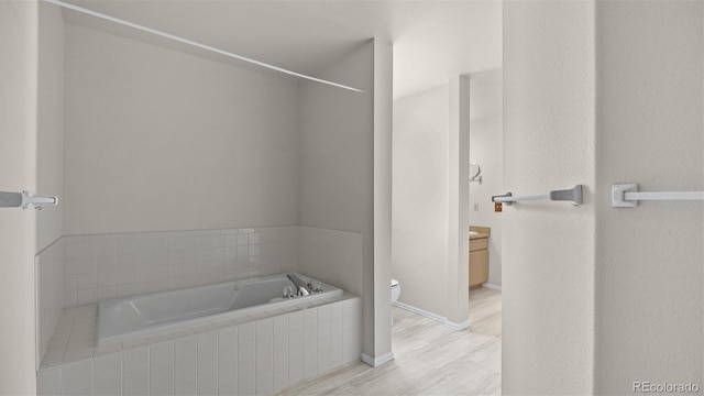 full bathroom featuring wood finished floors, tiled tub, vanity, and toilet