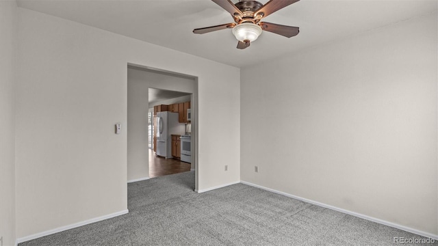 carpeted spare room featuring ceiling fan and baseboards