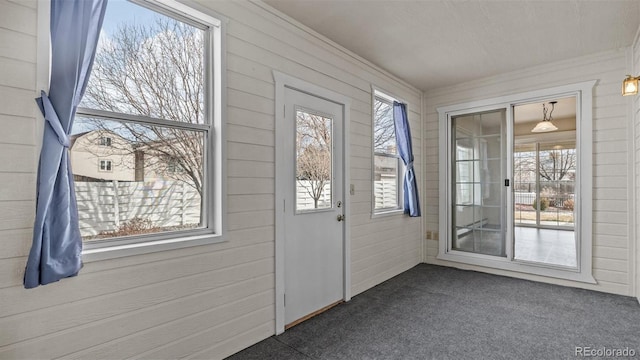 entryway featuring dark colored carpet, wood walls, and crown molding