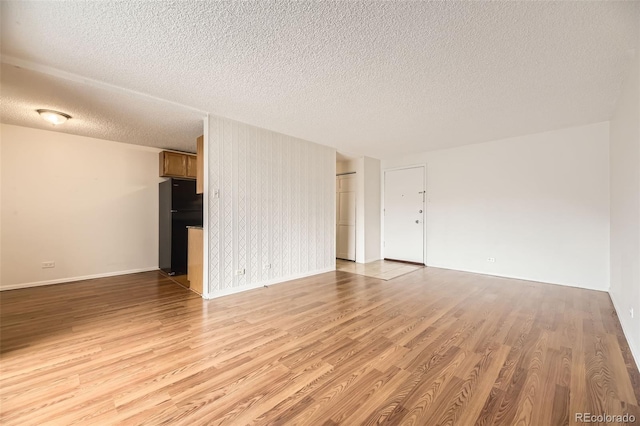 unfurnished living room with baseboards, a textured ceiling, and light wood-type flooring