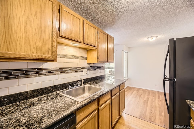 kitchen with decorative backsplash, a textured ceiling, light wood-style flooring, a sink, and freestanding refrigerator