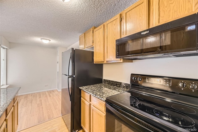 kitchen with a textured ceiling, baseboards, black appliances, light wood-style floors, and dark stone counters