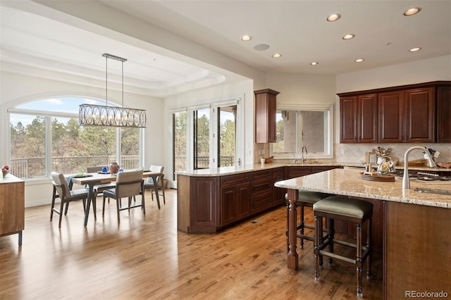 kitchen with sink, backsplash, hanging light fixtures, light hardwood / wood-style floors, and light stone countertops