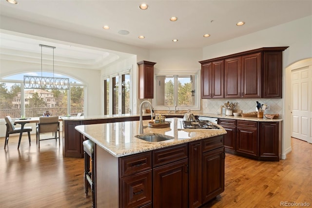 kitchen with sink, hanging light fixtures, stainless steel gas cooktop, a center island with sink, and light hardwood / wood-style flooring