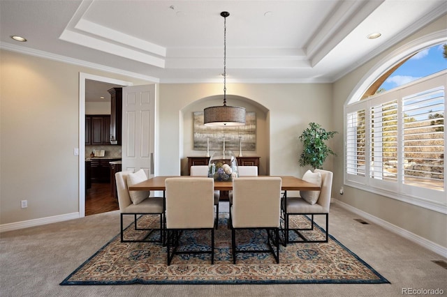 carpeted dining area with ornamental molding and a raised ceiling