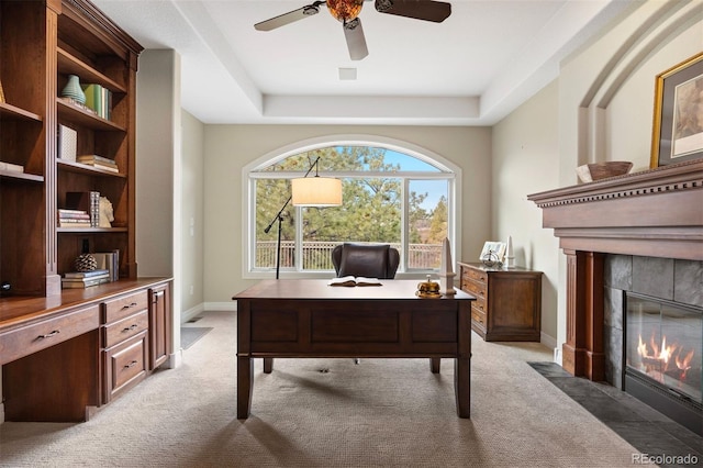 office area featuring ceiling fan, a tray ceiling, a tile fireplace, and light carpet