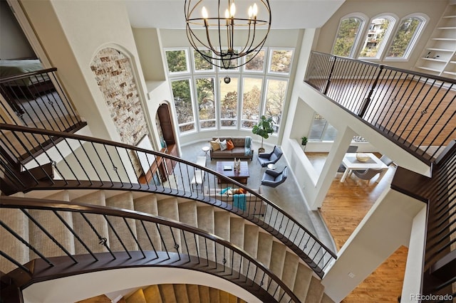 stairs featuring wood-type flooring, a towering ceiling, and an inviting chandelier