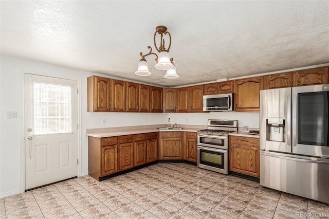 kitchen with a textured ceiling, a chandelier, pendant lighting, stainless steel appliances, and sink