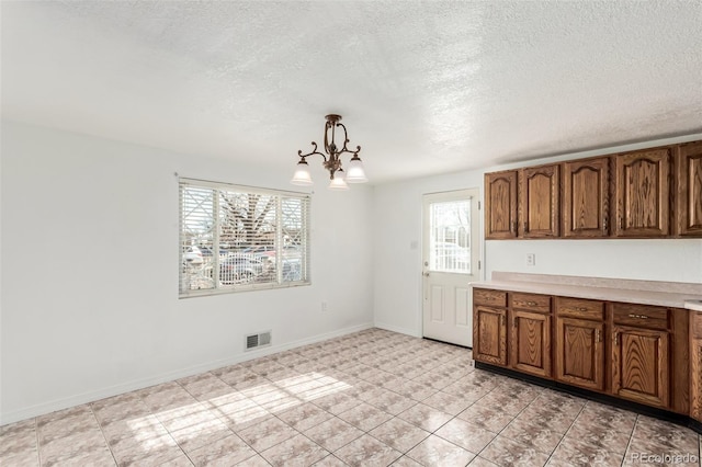 kitchen featuring a textured ceiling, a chandelier, light tile patterned floors, and pendant lighting