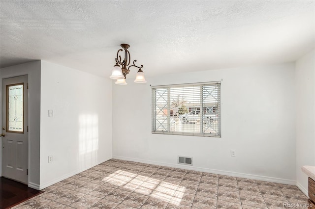 spare room featuring a textured ceiling and an inviting chandelier