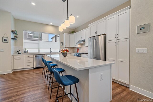 kitchen featuring a kitchen bar, appliances with stainless steel finishes, dark wood-style flooring, and white cabinetry