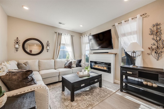living room featuring light wood finished floors, a glass covered fireplace, and recessed lighting
