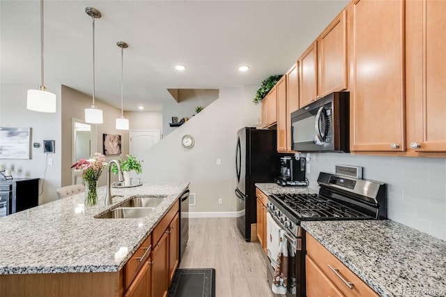 kitchen featuring appliances with stainless steel finishes, a sink, light wood-style flooring, a kitchen island with sink, and decorative backsplash