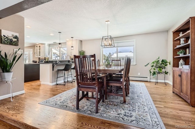 dining space with light wood-style floors, a wealth of natural light, a textured ceiling, and baseboard heating