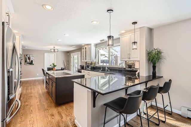 kitchen featuring a kitchen island, stainless steel fridge, a kitchen bar, glass insert cabinets, and pendant lighting