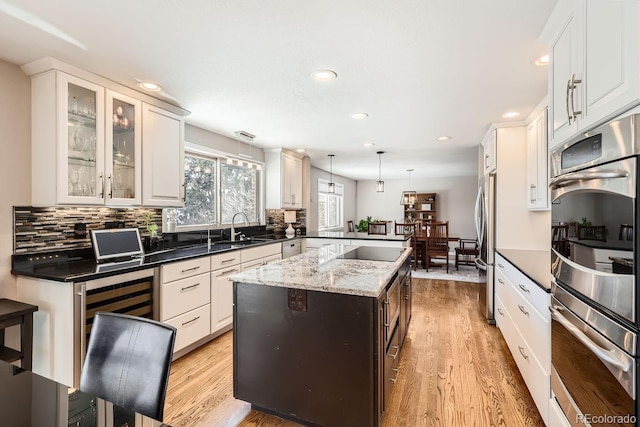 kitchen with glass insert cabinets, a center island, decorative light fixtures, stainless steel appliances, and a sink