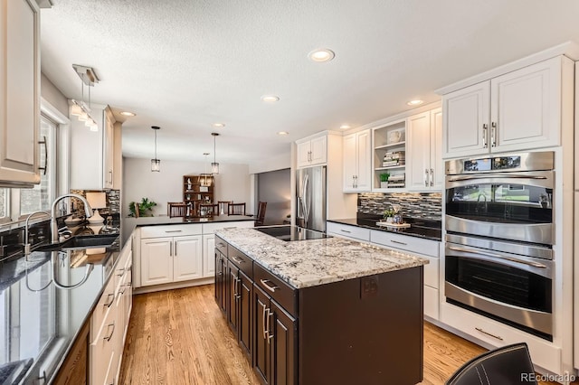 kitchen with a kitchen island, dark stone countertops, decorative light fixtures, stainless steel appliances, and a sink