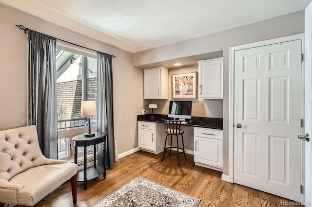 office with light wood finished floors, built in desk, a textured ceiling, and baseboards