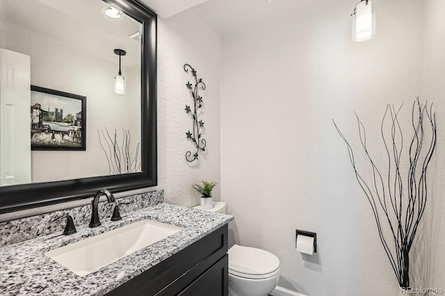 half bathroom with a textured wall, vanity, and toilet