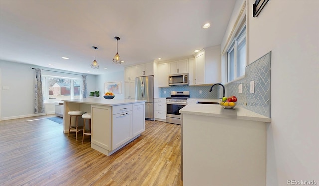 kitchen featuring a sink, a breakfast bar area, stainless steel appliances, white cabinetry, and a kitchen island