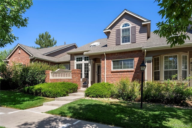 view of front facade featuring brick siding, a shingled roof, and a front lawn