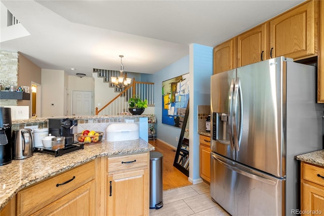 kitchen featuring light stone counters, a notable chandelier, stainless steel fridge, and pendant lighting