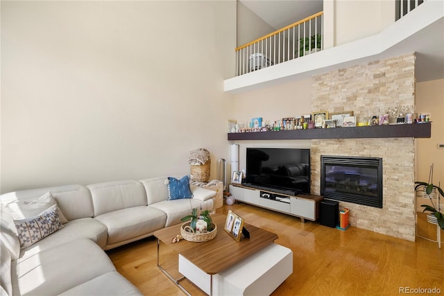 living room featuring a stone fireplace, wood finished floors, and a towering ceiling