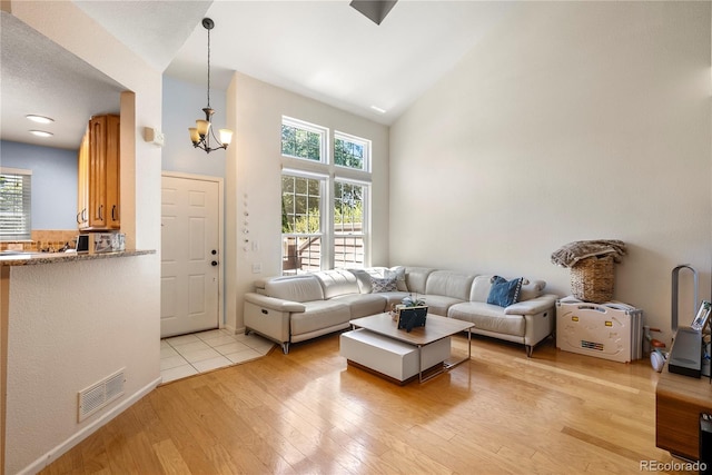 living room with a notable chandelier, visible vents, light wood-style flooring, and high vaulted ceiling