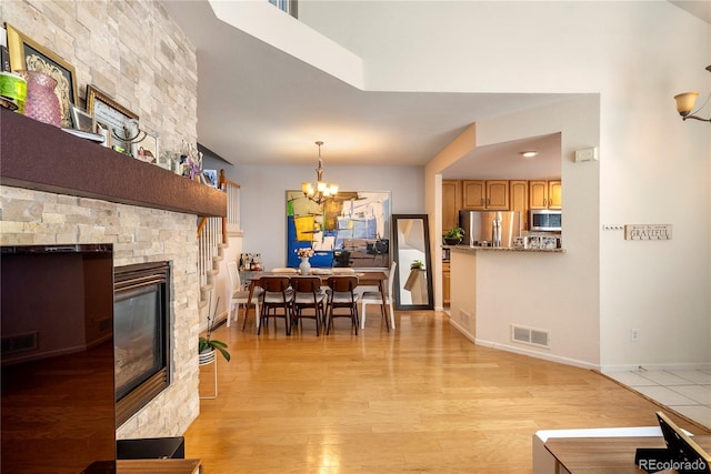 dining area with light wood-type flooring, visible vents, a stone fireplace, an inviting chandelier, and baseboards