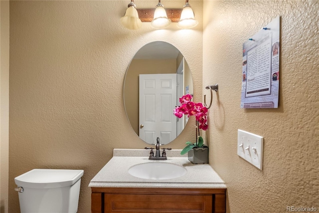 half bathroom featuring toilet, vanity, and a textured wall