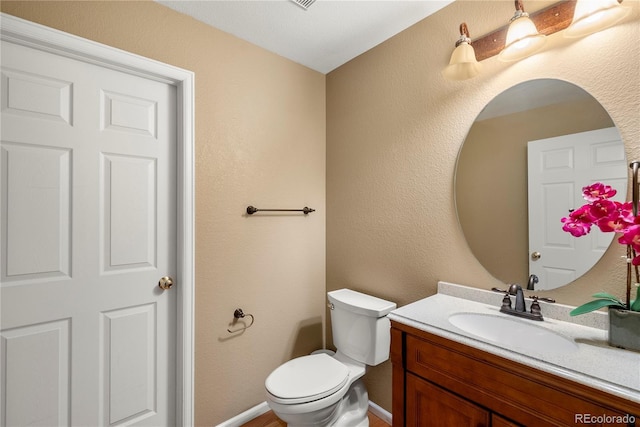 half bath featuring toilet, vanity, and a textured wall