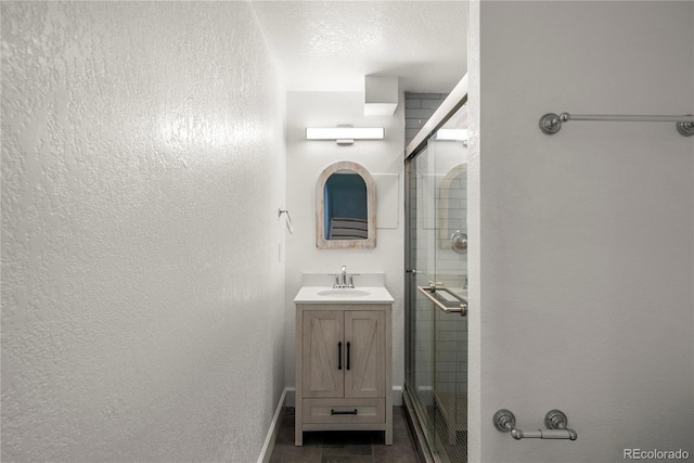 bathroom with vanity, a shower stall, baseboards, and a textured ceiling