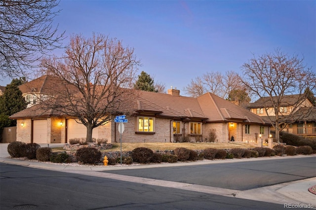 view of front of house featuring brick siding, a tiled roof, a chimney, and a garage