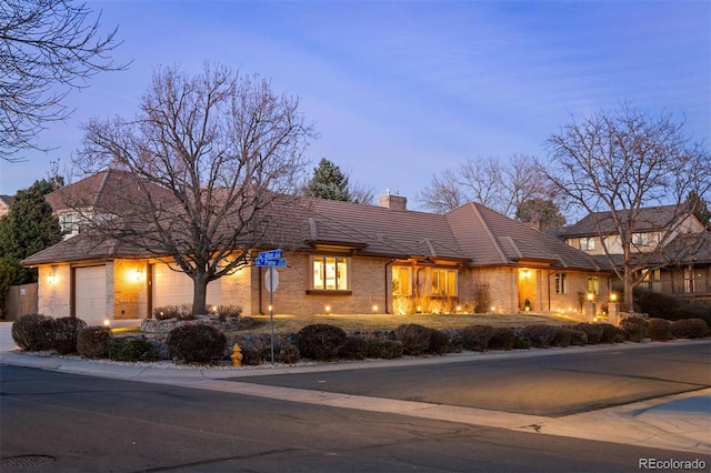 view of front of property featuring brick siding, an attached garage, and a chimney