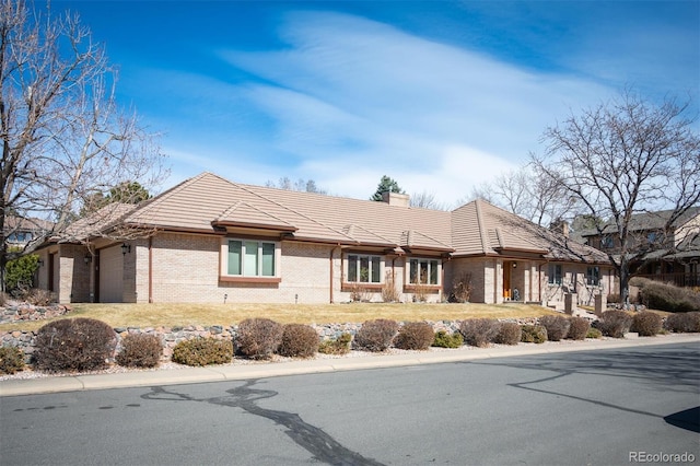 view of front of house with a tile roof, brick siding, a garage, and a chimney