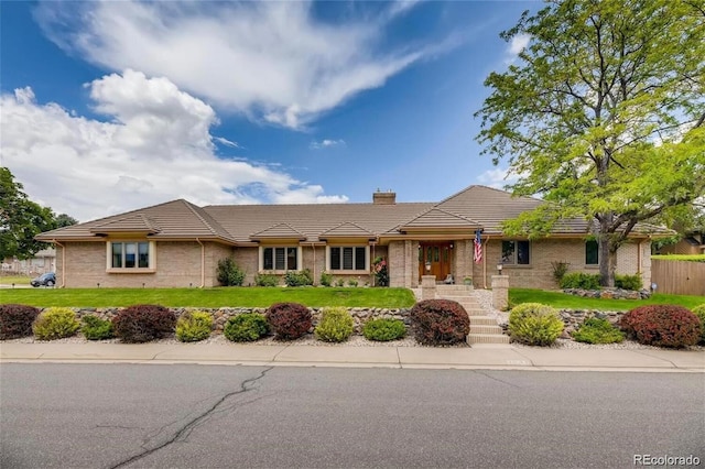 ranch-style house featuring brick siding, a chimney, a front lawn, and a tiled roof