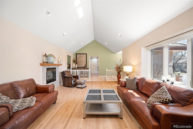 living area with high vaulted ceiling, wood finished floors, and a tiled fireplace