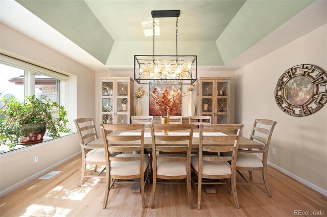 dining room featuring a tray ceiling, baseboards, light wood-style floors, and visible vents